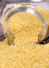 Millet groats spilling out of glass jar. Wooden background