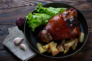 Frying pan with roasted pork knuckle, rustic wooden background