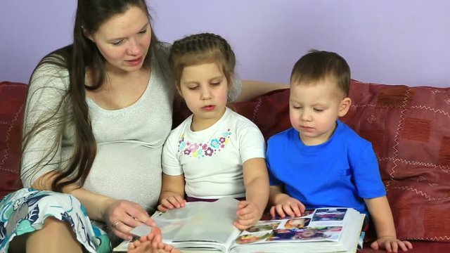 Mom with kids consider an album with photos. Happy family waiting for third child.