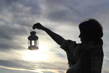 Girl silhouette with a candle lantern on backdrop of clouds and setting sun