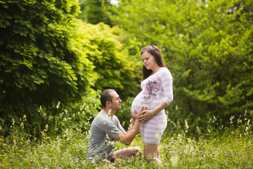 Happy couple waiting for baby. Man touches pregnant woman and hugs her belly outdoors in summer. New family concept. Paternity.