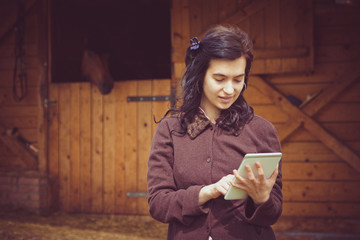 Female working on digital tablet in front of the stable     