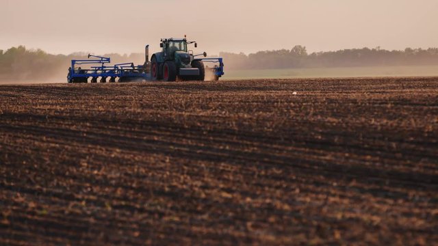 Tractor with drill goes through the field, carried out in spring seeding