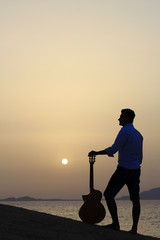 pensive man musician with his guitar at the beach watching the sunrise