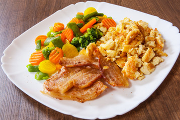 scrambled eggs with bacon and vegetables mix in a plate on wooden table