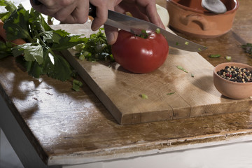 Chop celery, tomato, onions on a wooden cutting board for cooking.