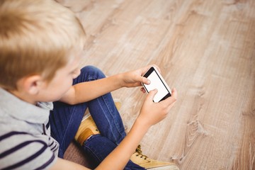 Boy using mobile phone while sitting on hardwood floor