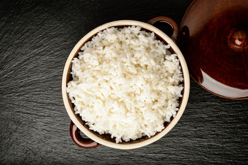 Boiled white rice in ceramic pot on black background.