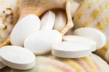 Fototapeta na wymiar Calcium natural food supplement pills on the seashells background, macro shot, selective focus