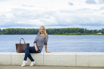 Fototapeta premium Young beautiful woman in blue jeans sitting in summer street par