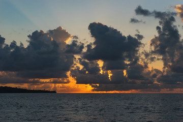 Sunset on a tropical beach - rays of sun make their way through clouds in the blue sky
