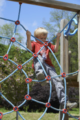 Fototapeta na wymiar Happy child boy climbed on top of the rope web on playground