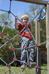 Happy child boy climbed on top of the rope web on playground