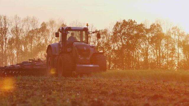 Tractor plowing a field in the rays of the setting sun