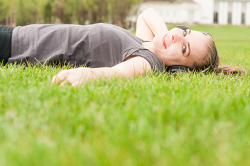 Relaxed female listening  music on earphones lying on grass