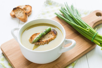 Bowl of asparagus soup with asparagus spear and bread on cutting