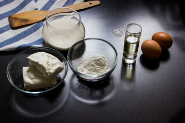ingredients for making cottage cheese dough (cottage cheese, flour, sugar, eggs, oil, salt) on a dark background
