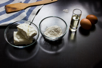 ingredients for making cottage cheese dough (cottage cheese, flour, eggs, oil, salt) on a dark background