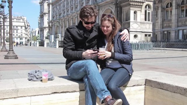 Happy Couple Having Fun With Smartphone Outdoors Hotel De Ville, Paris. Couple having fun with a smartphone in front of the famous Hotel De Ville in Paris, France
