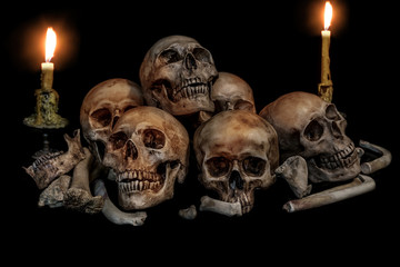 Pile of skulls and bones with two candles on black background. Genocides concept still life style.