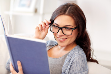 young woman in glasses reading book at home