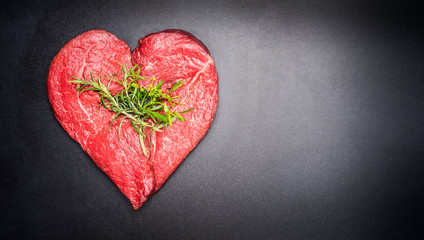 Heart shape raw meat with herbs on dark chalkboard background. Healthy lifestyle or organic food...