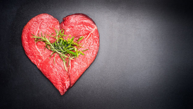 Heart shape raw meat with herbs on dark chalkboard background. Healthy lifestyle or organic food concept. For Meat lovers and eater