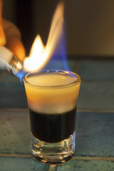 Lighter ignites B-52 cocktail - shooter - layered and with the flame on blue tiled bar - table.