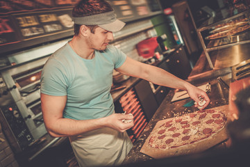 Handsome pizzaiolo making pizza at kitchen in pizzeria. - obrazy, fototapety, plakaty