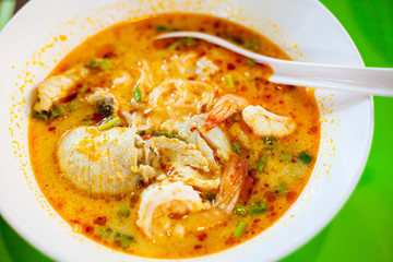 Noodle seafood hot and sour soup on white bowl with green background.