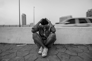 Asian young man with depression sitting beside street in a big c