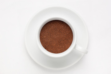 Coffee cup full of ground coffee on soucer against white background, top view