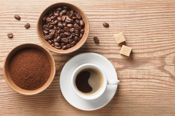Coffee beans, ground coffee and cup of coffee on wooden table decorated with cane sugar cubes and coffee beans, top view