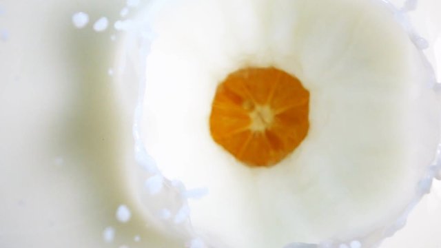 The half of juicy orange drops in fresh white milk with stunning splash in slow motion. Camera vertical shooting with 500 frames per second speed.