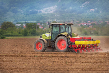 Farmer in tractor sowing crops at field with seed scattering agr