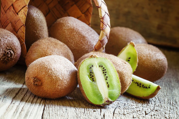 Kiwifruit poured out of a wicker basket, vintage wooden backgrou