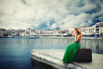 Woman sitting on a suitcase on a pier talking on mobile phone waiting for the boat