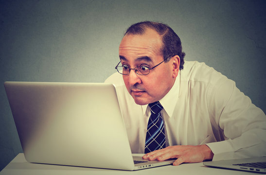 middle aged shocked business man sitting in front of laptop computer looking at screen