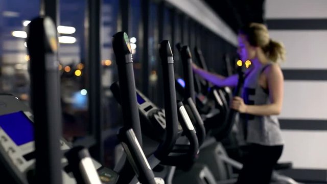 view of emty gym with one girl on elliptical trainer working hard