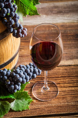 Fresh wine in glass with grapes on wooden barrel
