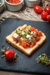 Grilled toasted bread with roasted tomatoes, feta cheese and radish sprouts.