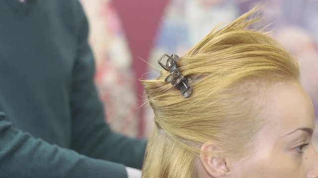 Professional barber divide hair of blonde girl on parts, fixing by bobby pin in beauty saloon. Hair Styling. 
