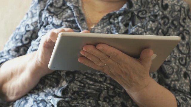 Old woman looks at photos using a digital tablet