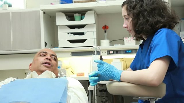A young intern talks to a patient sitting in the dental chair as they wait for the dentist to enter.