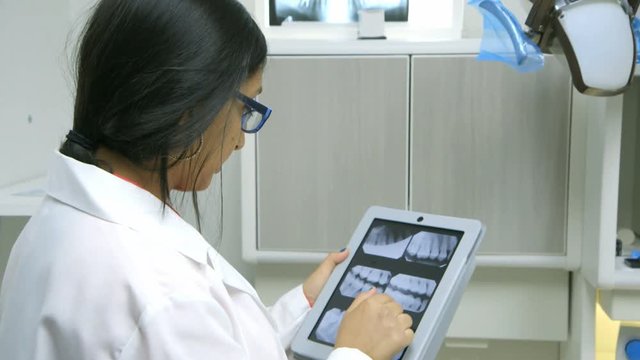 A young female dentist or intern reviewing dental x-rays on an electronic table turns and smiles.