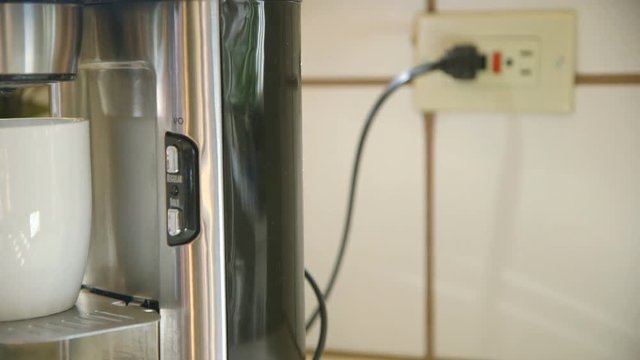 An environmentally conscious woman saves energy by unplugging the coffee maker after her coffee is ready.