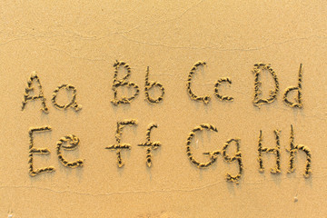 Alphabet written by hand on sandy beach (letters from A to H)