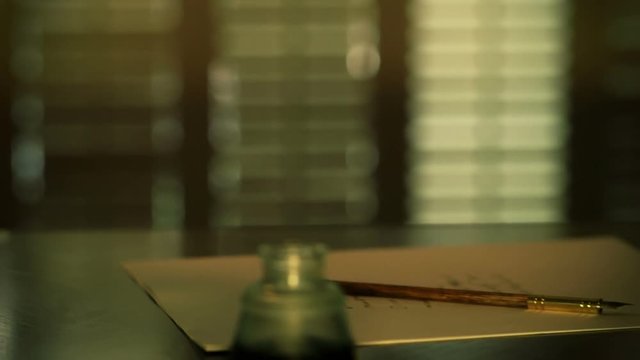 Scene moves down an old oil lamp to an inkwell and dip pen lying unused on a desk.