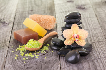 Spa setting with bath salt, soaps, loofah and black stones on wooden background 