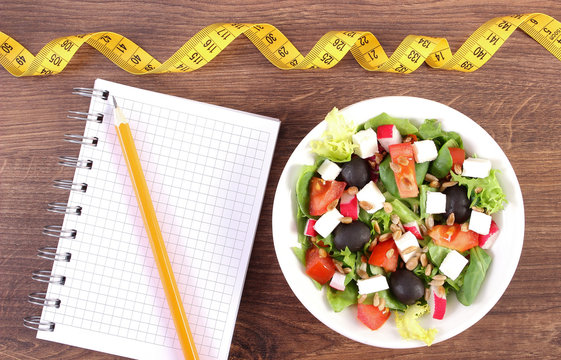 Fresh greek salad with vegetables, centimeter and notepad for writing notes, healthy nutrition and slimming concept
